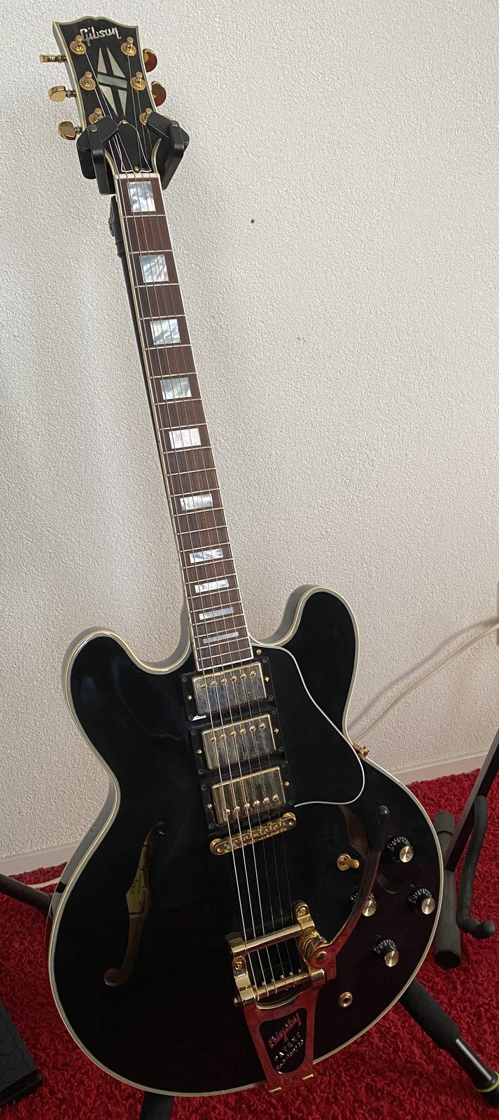 Gerbman's black Gibson ES-355 Custom Shop on a stand at home — three gold humbuckers, gold Bigsby vibrato