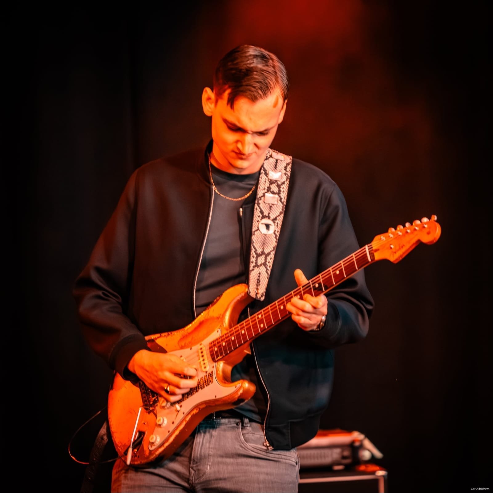 Gerbman close-up with sunburst relic Stratocaster under red stage light, snake skin guitar strap — photo Ger Adrichem