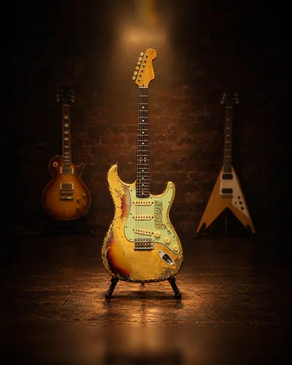 Stratocaster relic Aztec Gold en un soporte, con una Les Paul y una Flying V detrás